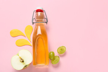 Bottle of fresh apple juice with grapes and splashes made of paper on pink background