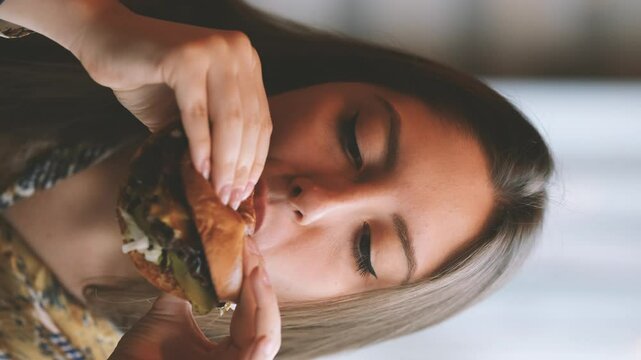 Close-up portrait of a woman in a fast food cafe eating a hamburger. Hungry woman eating a burger.