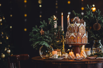 Family holiday celebration. Beautiful traditional homemade gingerbread house. Celebration of Christmas and Happy new year at home. Festive mood, cozy atmosphere, burning candles, fir tree branches