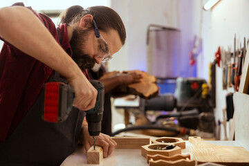 Man in carpentry shop wearing protection gear while drilling holes into wood to prevent workplace accidents. Cabinetmaker equipped with safety glasses while using power drill to avoid injury