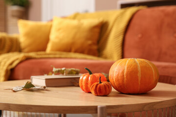 Pumpkins with autumn leaves and book on coffee table in stylish living room, closeup