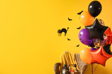 Colorful balloons with Halloween decorations on wicker armchair against yellow background