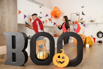 Young happy couple with word BOO decorating wall for Halloween party at home