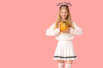 Beautiful young happy woman in headband with Halloween pumpkin and paper spider on pink background