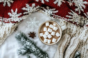 Flat lay of snowflakes, mittens, a wool scarf, a cup of hot cocoa with marshmallows, and pine branches 