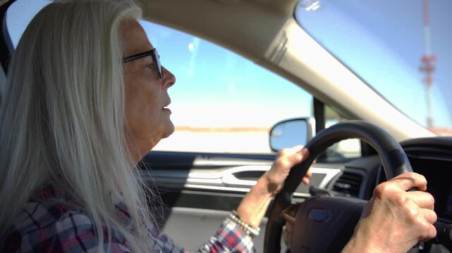 Old woman drive a car in hot and sunny day on highway. A woman with glasses is driving a car at deserts area during sunshine. Uber driver driving in beautiful place