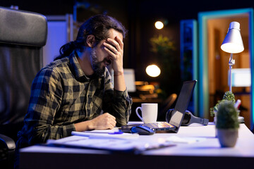 Male freelancer, holding his head with a visible headache, conveying emotional stress and...