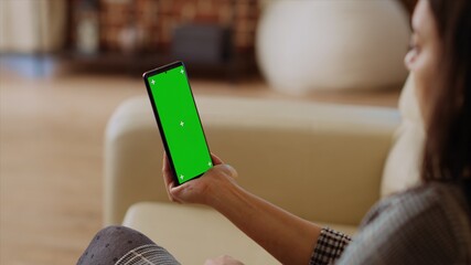 Woman using green screen smartphone gyroscope function while sitting on cozy couch at home. Person...