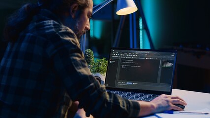 Skilled computer scientist writes code on laptop screen while in living room office using...