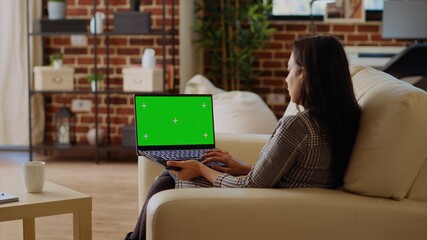 Self employed woman staying at home using green screen laptop to do various job tasks from couch....