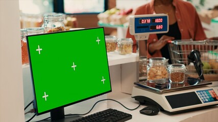 Merchant selling goods next to pc with greenscreen at checkout, locally grown fruits and veggies for sustainable lifestyle. Computer monitor running isolated chromakey display and mockup.