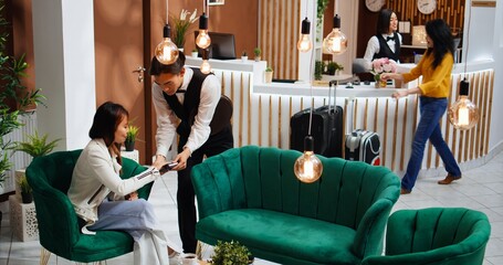 Young traveler ordering coffee cup and paying with card, man serving drink and holding pos terminal to process payment. Asian person enjoying luxurious services from five star hotel staff.