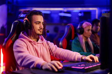 Gamer guy with headset sitting in gaming room and playing online rpg.