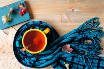 Autumn background - cup of tea, book and warm scarf on the wooden background. Autumn background, with concept of spending autumn time at cozy home
