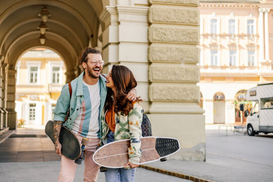 Romantic hipster couple with skateboards laughing and hugging on street