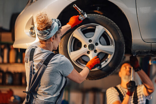 Rear view of female auto mechanic fixing car wheel at mechanic workshop