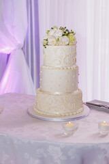 White three-tier cake decorated with roses for the wedding banquet of the bride and groom. Luxurious birthday cake on a table in a restaurant