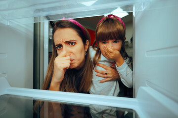 Mother and Daughter Covering Noses Because of Stinky Fridge. Family complaining about the bad smell coming from the refrigerator 
