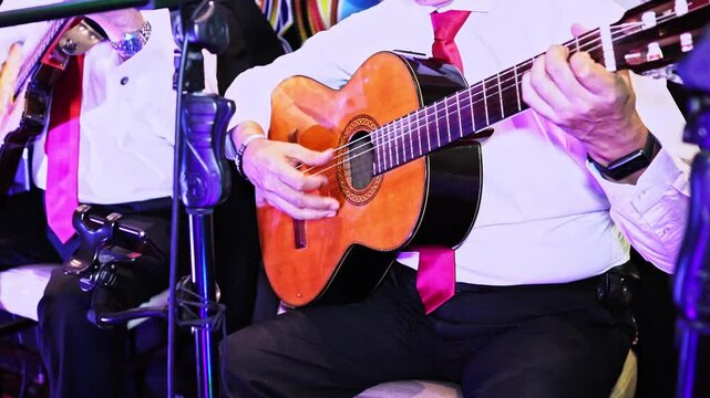 gentleman playing acoustic guitar, accompanied by an orchestra. detail shot.