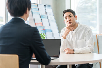 保険の相談に来た中年男性と接客対応する男性ビジネスマン
