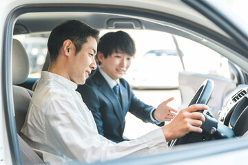 ショールームで自動車の車内で営業マンの説明を受ける顧客の男性
