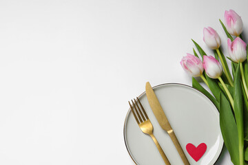 Table setting for romantic Valentine's day celebration, top view. Plate, cutlery, heart and flowers on white table, space for text