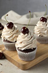 Delicious cupcakes with cream and cherries on light textured table, closeup