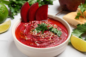 Tasty beetroot hummus in bowl and products on white table, closeup