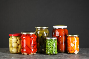 Different pickled products in jars on grey textured table