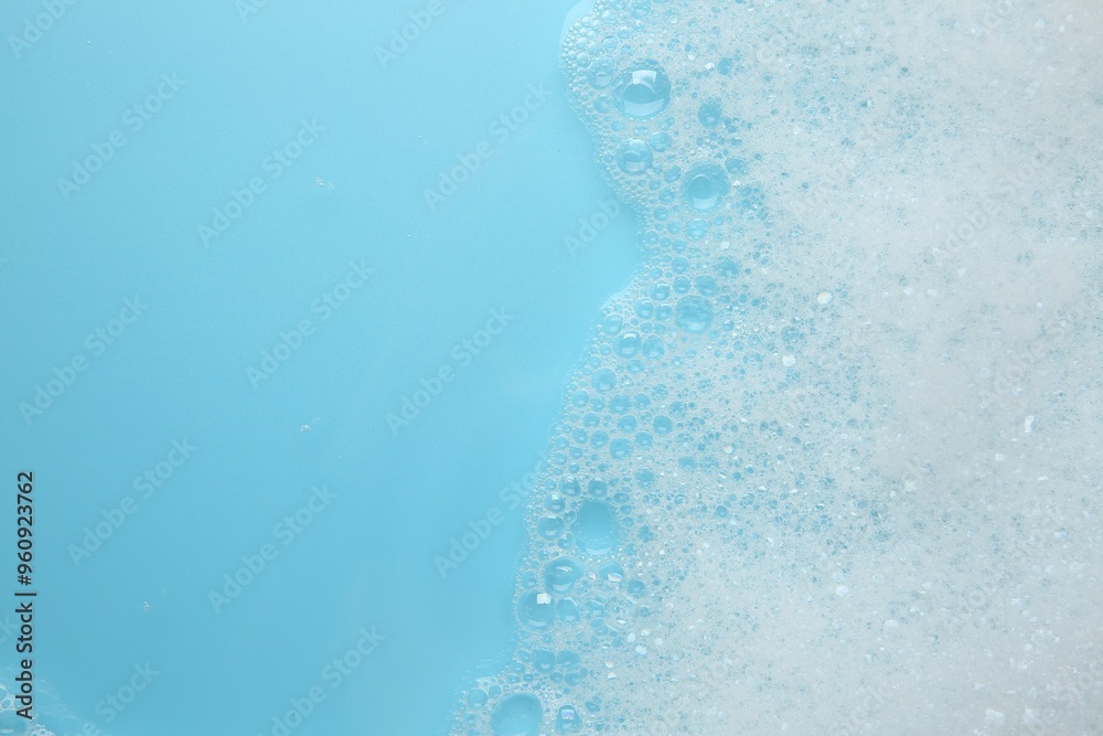 Wall mural Washing laundry. White foam with bubbles on light blue background, top view. Space for text