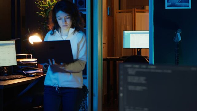 Computer scientist walking at home, developing software applications using laptop. IT professional standing in living room, implementing and maintaining company systems, camera A