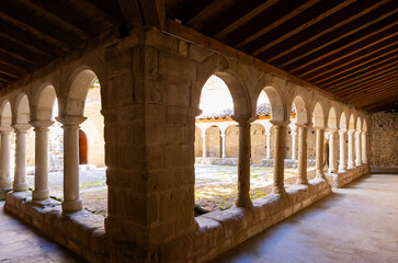 Serene shaded gallery at Sant Llorenc de Morunys with ancient stone columns and arches surrounding...