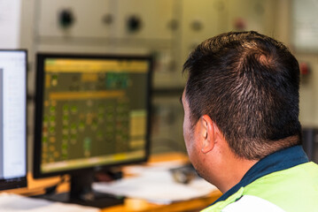 A marine engineering officer is seated in the Engine Control Room, focused on the monitors in front of him, diligently overseeing the operational parameters of the ship's machinery. 