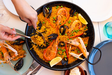 Hostess of house circumcised hands shift sea paella into serving plates, family dinner is served....