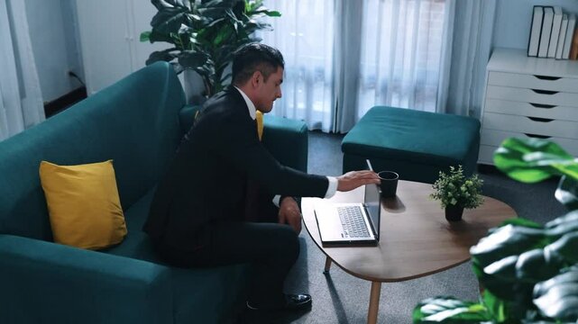 Stressful boss look at decrease sales from laptop and lies on sofa. Professional tired project manager working laptop while feeling stress. Skilled business man having headaches at work. Directorate.