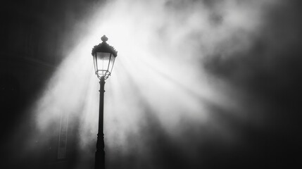A lamp post casting light on a foggy street, with the light beams visible in the mist.