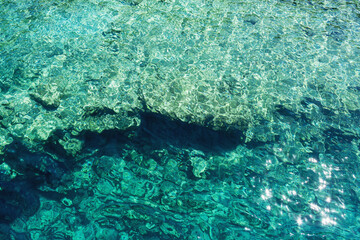 A stunning display of clear turquoise water, creating mesmerizing light patterns as sunlight pierces through, revealing both the depth and clarity of the sea below. Pure natural beauty