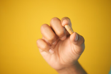 holding a herbal medicine capsule against yellow background 