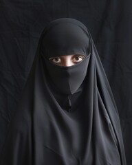 Naklejka premium Close up portrait of young, adult woman in black burqa with hidden face, isolated on black background.