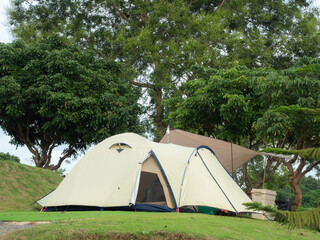 Cream Dome tent pitched on grassy field, mountainside grass field with a few trees in background. Some clouds in sky. Holiday activities