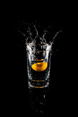Water splash from inside orange drink glass on black background