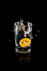 Water splash from inside orange drink glass on black background