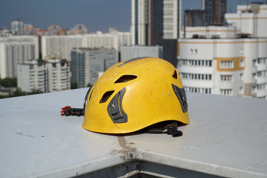 A climber's helmet lying on the parapet of a high-rise building's roof against the backdrop of a city.