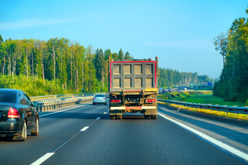 Dump truck drives along a road among other vehicles surrounded by forest.