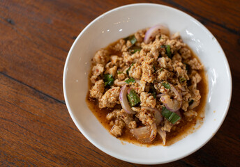 Pork larb in a white plate placed on a wooden table with space to copy and use.