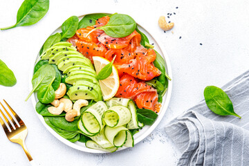 Keto salad with salmon, avocado, spinach, cucumber, sesame seeds  and cashew nuts.. White background, top view