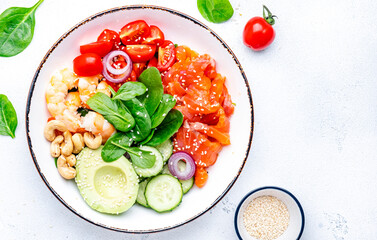 Seafood salad poke bowl with shrimp, salmon, avocado, spinach, cucumber, tomato, cashew, sesame seeds. White background, top view