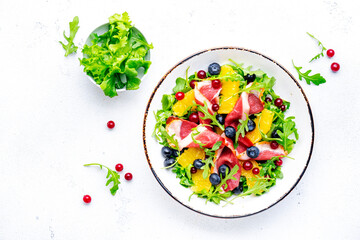 Delicious salad with smoked duck fillet, juicy orange, fresh blueberries, cranberries and arugula on white background, top view