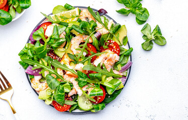 Fresh green salad with avocado, shrimps, tomatoes, arugula, lamb lettuce, onion and sesame seeds on white background. Top view