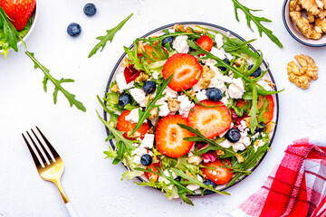 Strawberry and feta salad with arugula, lettuce, blueberries, cheese and walnuts, white background, top view